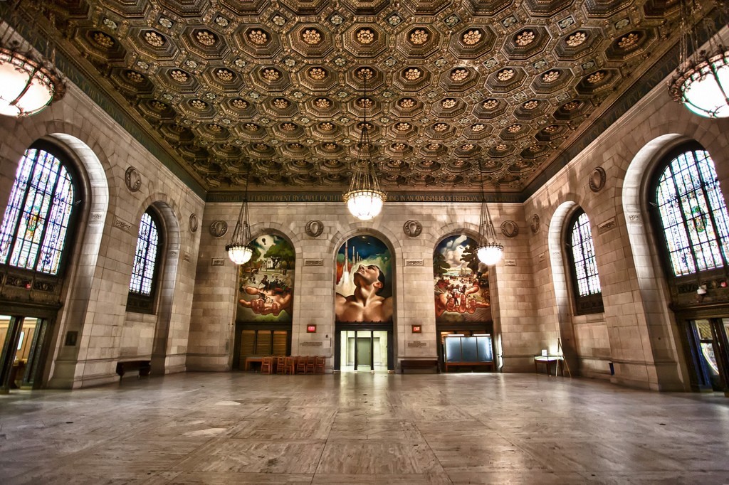 Adam Strohm Hall, a grand room with high intricately coffered ceilings and a set of three murals titled "Man's Mobility" on the far wall.
